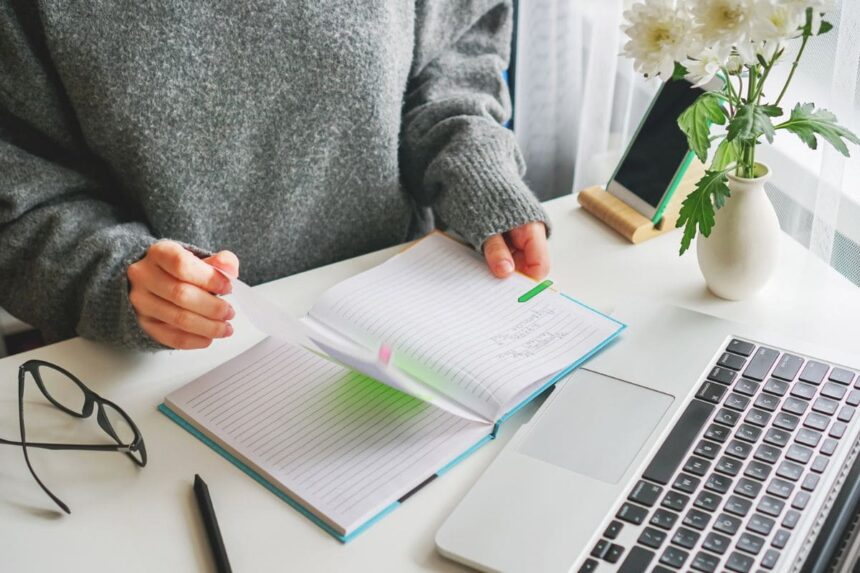 A woman working from her home office at a desk and flipping through a planner.