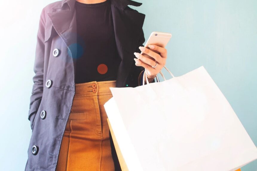 A woman holding a cell phone and bags in her hands as she shops.